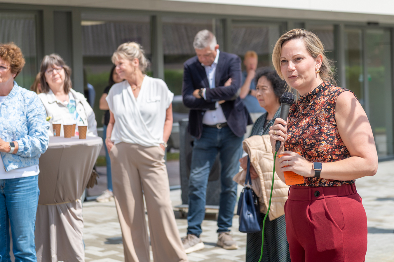 Locatiemanager in rode broek met gebloemde top geeft een speech tijdens de opening.